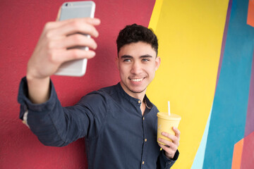 Smiling man with disposable up taking selfie against colorful wall