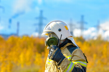 A firefighter rescuer in a protective suit, gas mask and white helmet extinguishes a fire at a...