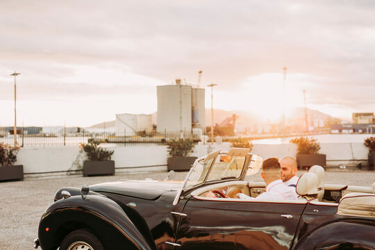 Elegant gay couple in a vintage convertible car at sunset