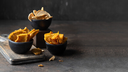 Assortment of natural snack on dark background.  Dried fruit slices of mango, pineapple, apple into the black bowls. Large image for banner