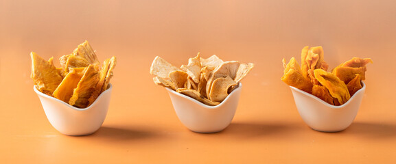 Different dried fruit  slices, mango, pineapple, apple into white bowls at beige background....
