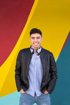Happy young man with hands in pockets standing against multi colored wall