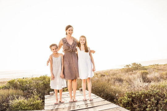 Happy mother embracing her two daughters on a boardwalk at sunset