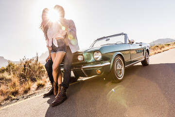 Couple embracing at convertible car on a country road in backlight