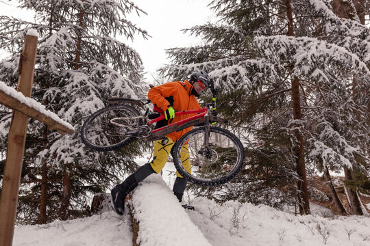 Man with mountainbike crossing fallen tree on path in winter forest