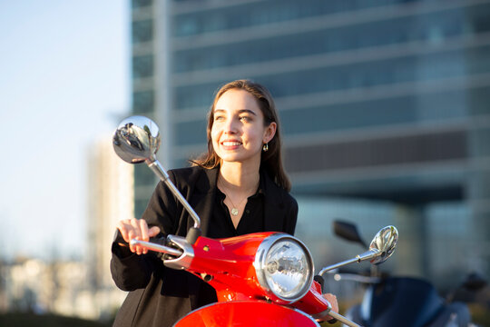 Smiling businesswoman looking away while sitting on motor scooter during sunset