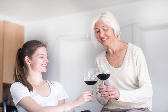Mother and daughter in the wheelchair with a glass of red wine at home