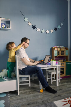 Man working and using laptop in children's room with simultaneous childcare