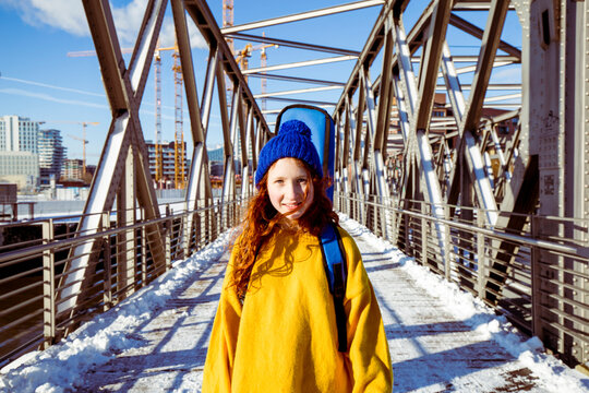 Smiling girl with guitar standing on bridge against sky during winter
