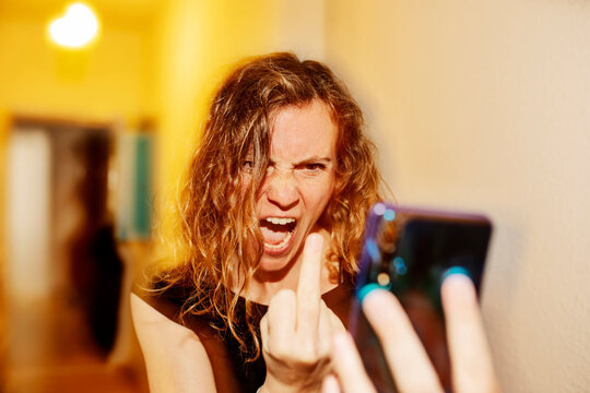 Close-up of aggressive woman showing middle finger on video call over smart phone at home