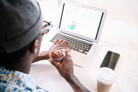 Man using laptop while eating muffin at home