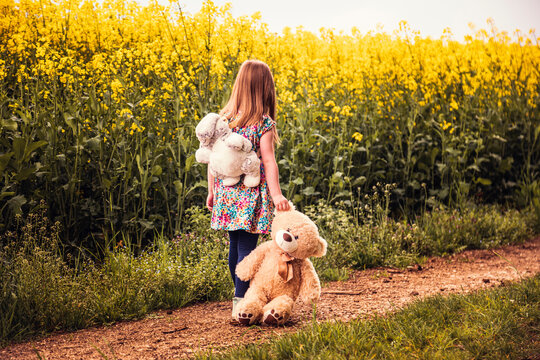 Girl walking alone with teddy and backpack on a field way