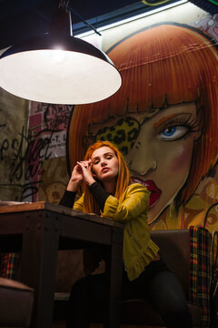 Portrait of redheaded young woman waiting in a pub in front of graffiti wall