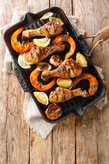 Grilled chicken legs with seasonal vegetables close-up in a grill pan on the table. Vertical top view from above