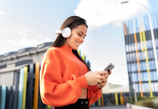 Portrait of beautiful brunette standing outdoors and smiling while listening to music on headphones