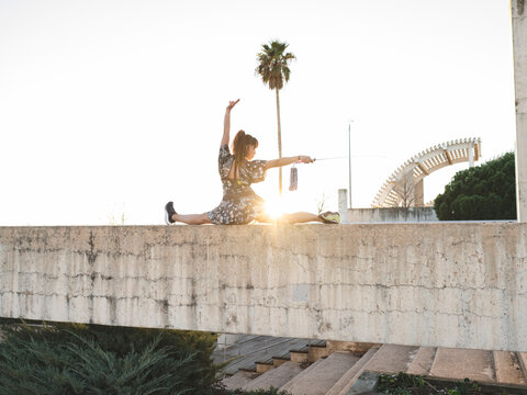 Young female athlete doing split on retaining wall in sunlight