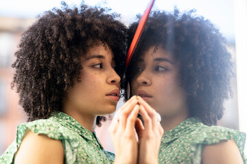 Young afro woman looking at reflection in glass wall