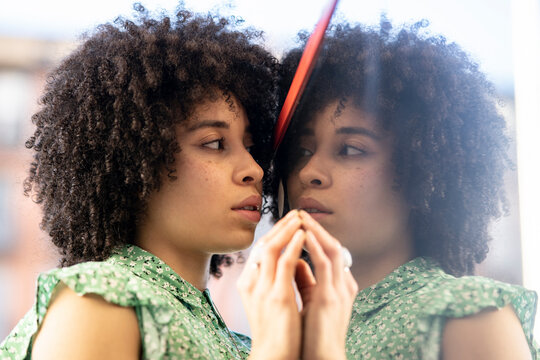 Young afro woman looking at reflection in glass wall