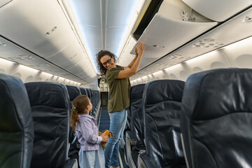 Happy woman folding luggage and looking at her daughter on the plane. Travel and family concept