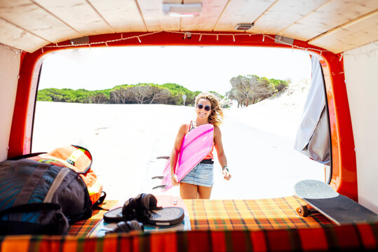 Woman standing while holding surfboard in front of trunk