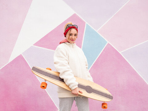 Smiling woman holding skateboard while standing against multi colored wall