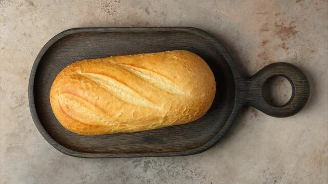 Stop motion. A loaf of bread on a cutting board is cut into slices. The cutting board comes in and out of the frame. Food concept.