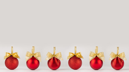 Bright New Year background - shimmer red balls with gold bows stand in row as pattern border on soft light white table in minimal style, copy space. For design of poster, flyer, card, brochure.