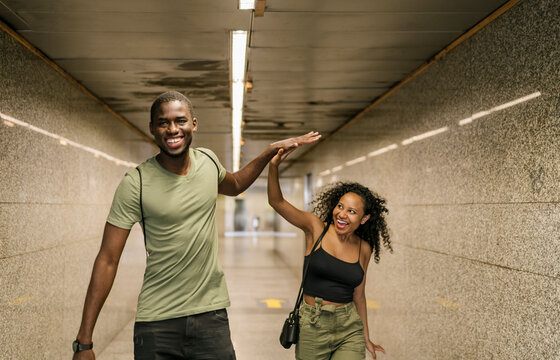 Cheerful couple giving high-five while walking in underground walkway at subway station