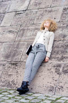 Fashionable blond woman with folder leaning against wall having a rest