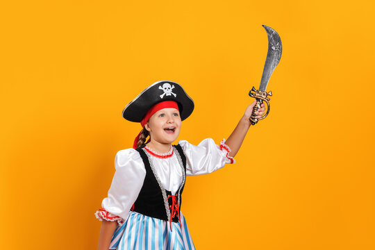 Halloween. Cheerful little girl in a carnival costume of a pirate in the studio on a colored yellow background. The child is holding a saber.