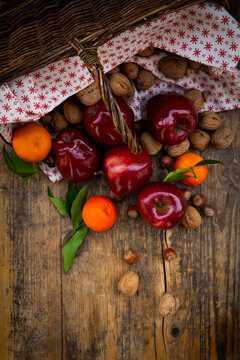 Wickerbasket, red apples, tangerines, hazelnuts and walnuts on dark wood