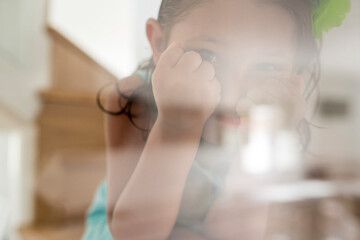 Close-up of cute girl looking through glass at home