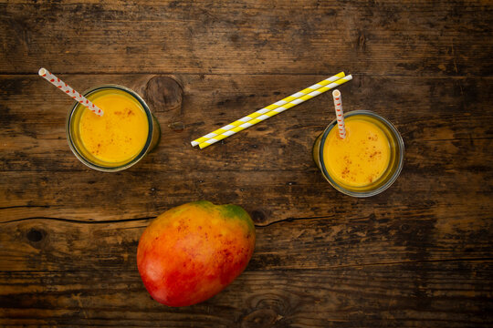 Mango and two glasses of Mango Lassi with curcuma and straws on wood