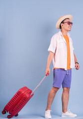 Young Asian man holding red suitcase on blue background