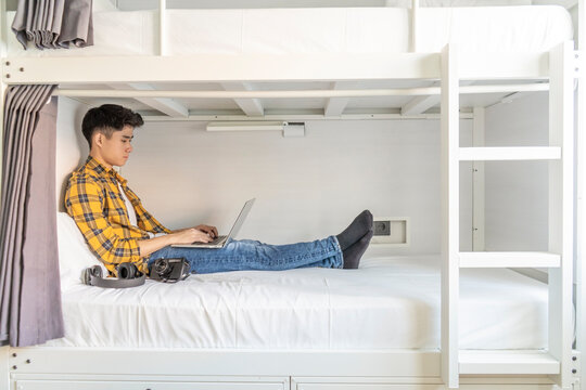 Young tourist sitting on bed in a hostel using laptop