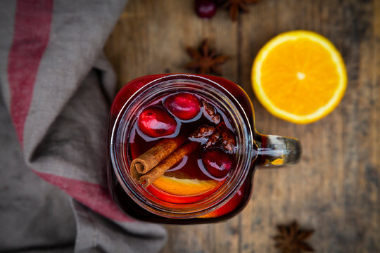 Glass of mulled wine with cranberries, cinnamon sticks, orange and star anise on dark wood, focus on foreground
