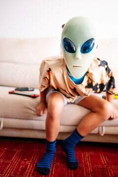 Boy wearing alien mask sitting on sofa at home