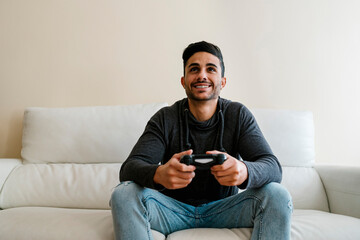 Smiling young man sitting on sofa while playing video game at home