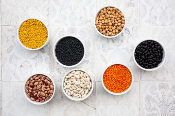 Various legumes in bowls: chickpeas, cannellini beans, quail beans, black beans, yellow lentils, red lentils, black lentils