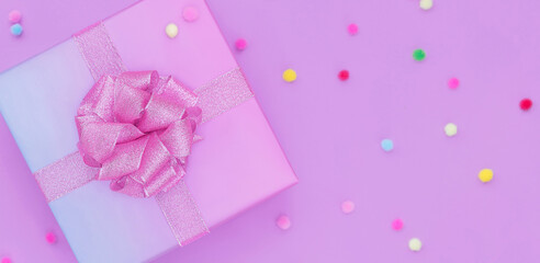 gift box with a pink bow on a pink background with colorful pompoms