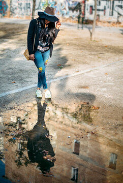 Woman standing by puddle with her reflection on road