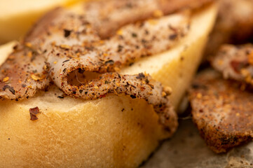 Sliced homemade bacon with pepper and sliced bread, close-up, selective focus.