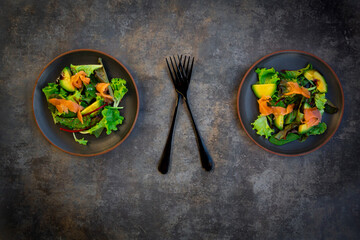 Plates of green salad with corn salad, arugula, spinach, red leaf lettuce, beetroot leaves,ÔøΩavocado, salmon meat and balsamic vinegar