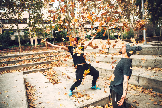 Young friends playing with autumn leaves in public park