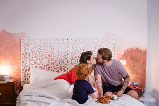Parents kissing while having breakfast with son bed at home