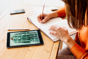 Female fashion designer working at home sitting at desk with tablet taking notes