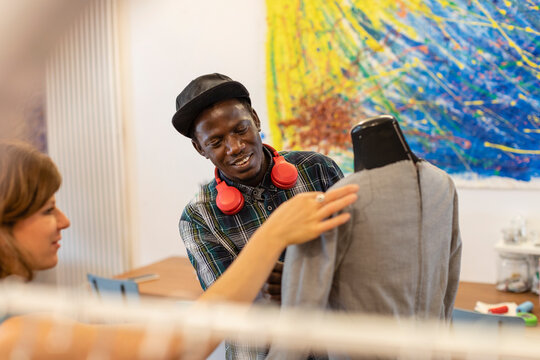 Smiling young man looking at fashion designer holding mannequin in design studio