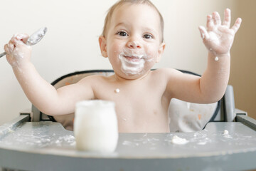 Little baby boy eating yogurt in highchair at home