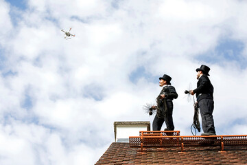 Two chimney sweeps on house roof looking at drone