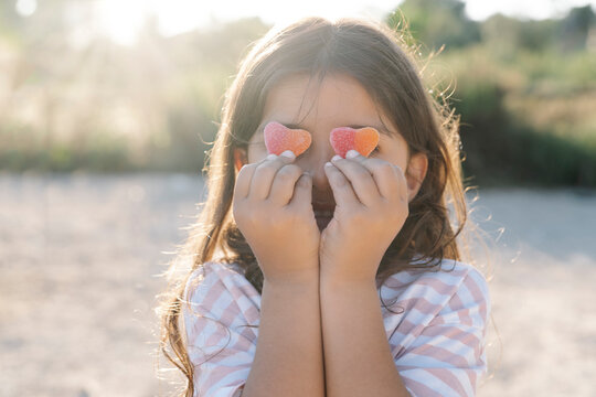 Close-up of cute girl holding candy hearts against face at park during sunset